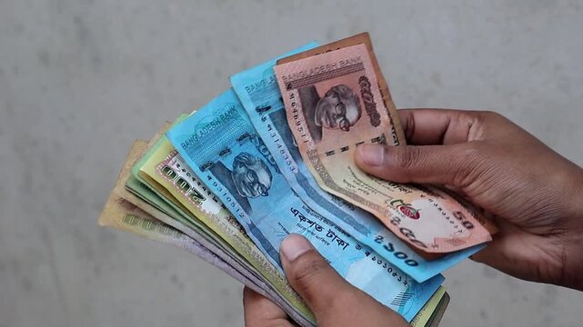 Detailed shot of counting Bangladeshi Taka money, including 50 and 500 notes, for business or personal use. This sequence shows a person handling paper currency for financial stability concepts.
