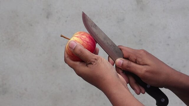 Close-up of human hands about to slice a ripe gala apple using a stainless steel knife outdoors. It is perfect for food blogs, nutrition guides, and organic lifestyle marketing content.