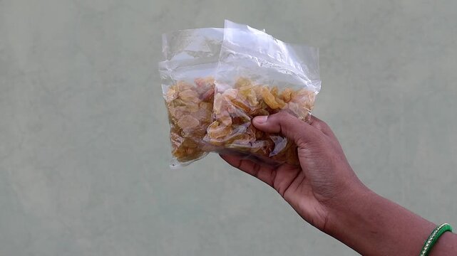 Close-up of a person's hand holding two plastic bags filled with golden raisins. This footage represents bulk purchase, healthy snacking options, and natural energy food products.