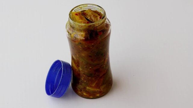 Close-up of traditional spicy mango pickle in a transparent glass jar with an open blue lid. This shot highlights authentic South Asian condiments, homemade preserves, and tangy flavors.