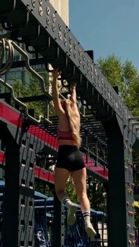 A steady low view follows a woman in sportswear passing under outdoor gym bars, with trees and open sky shaping the background. The scene evokes movement, wellness, discipline, and everyday fitness.