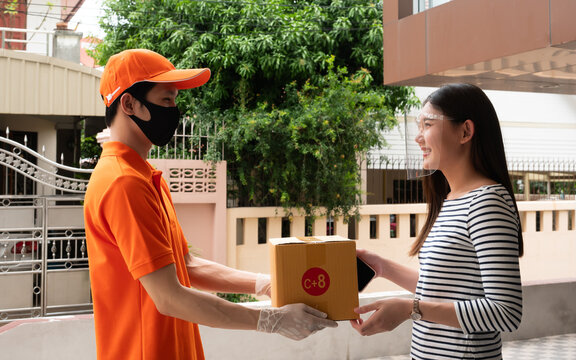 Asian Courier Delivering Parcel Box to Female Customer at Home Entrance, Contactless Delivery Service with Face Mask and Face Shield During Modern Online Shopping Lifestyle Scene