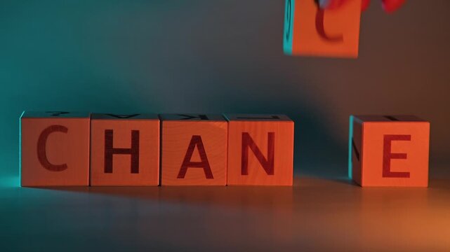 The action shows a person allowing letters to change positions to form the word CHANGE. The focus is on the movements of the hand as it manipulates the blocks in a well-lit area