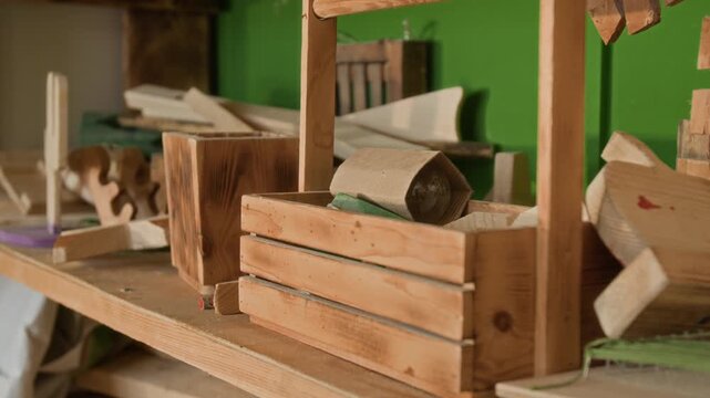 Close-up shot of pieces of scrap wood and small wooden crate with light bulb on workshop table, with green wall in background