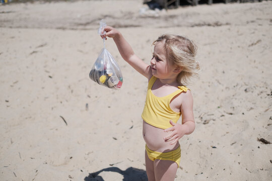 Little girl volunteer collecting plastic waste and garbage in bag on the sandy city beach