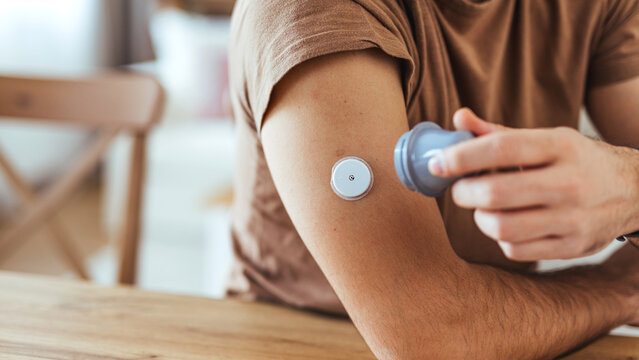 Man Checking Continuous Glucose Monitor Sensor on Arm at Home &mdash; Diabetes Care and Health Monitoring