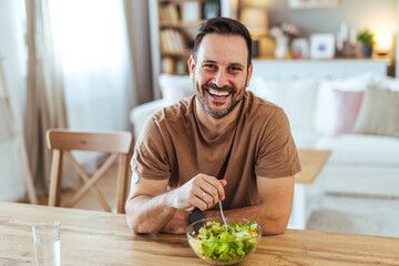 Fototapeta premium Smiling Man Eating Healthy Salad At Home Kitchen Table Enjoying Casual Lunch