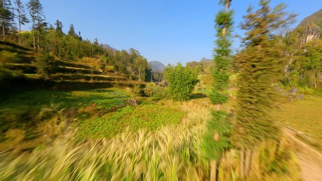 Cinematic FPV drone flight above rural fields and valleys in Ha Giang, Vietnam. Fast aerial movement through scenic farmland, limestone hills, and mountain countryside in northern Vietnam.
