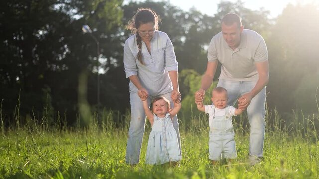 baby first steps. family walking in the park. mom and dad teach two babies the first steps on grass in the park. happy family kid dream concept. family and baby walk in the park in summer lifestyle