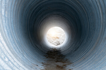 Fototapeta premium Concrete tunnel leads to bright, open sky above. Wet walls show signs of use and time. Dirt stains the floor, hinting at recent passage. View invites curiosity, exploration, or escape