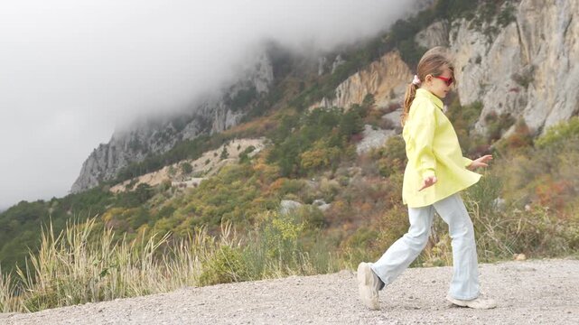 Girl, mountains, clouds. Happy girl exploring high mountain trails dancing under heavy fog and dramatic cloudy sky.