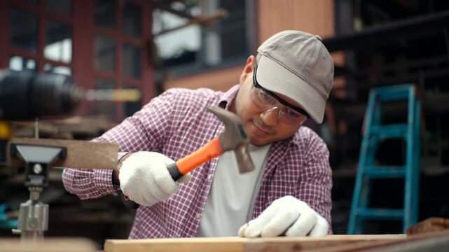 Confident carpenter man hammering nail into wood inside timber workshop. DIY woodworking, handmade furniture, home improvement and craftsmanship concept.