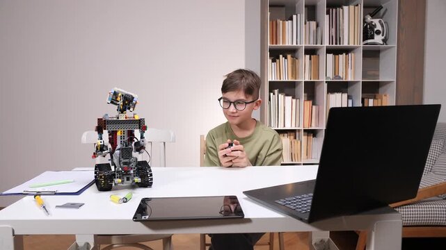 Young boy learning stem subjects by building and programming a block based robot on a table with a laptop, tablet, and tools, demonstrating modern educational technology and skill development