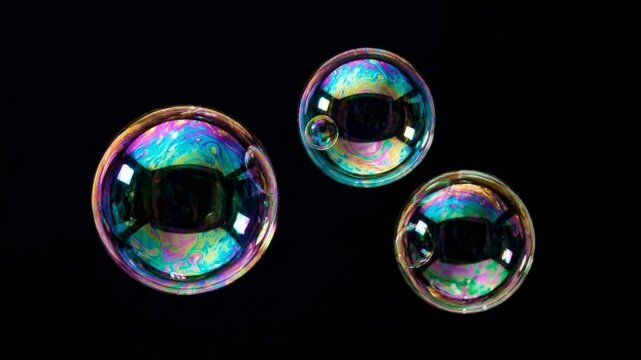 Close up of three colorful soap bubbles floating in the air against a black background