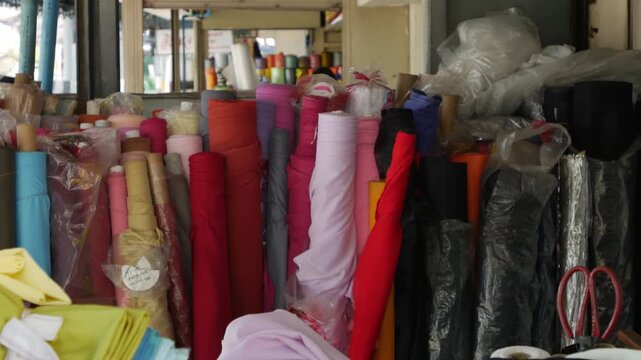 Vibrant colorful fabric bolts and textile rolls stacked at cloth market with rainbow of materials for garment making