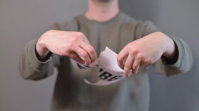 A person holds a piece of paper that has text about an AI bubble. After displaying it, they tear the paper and point to the camera, indicating various ideas related to technology