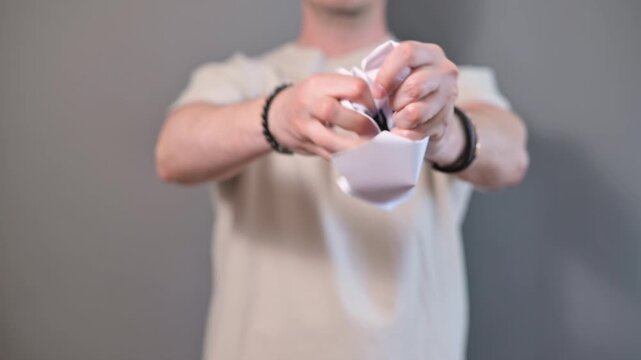 An individual holds a sign displaying the word SHAME in a minimalistic environment. The person, a young adult male, then crumples and discards the sign, symbolizing a personal struggle with emotions