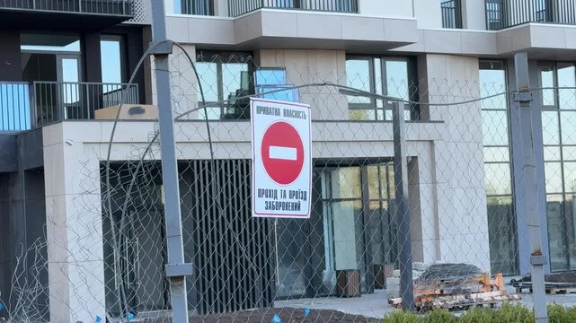 Private property warning sign with no entry traffic symbol on wire fence near modern residential construction site and newly built apartment building