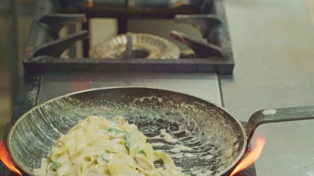 Champignon mushrooms are being stirred in a frying pan on a stove. The action takes place in a cozy kitchen, creating a delicious dish. Close-up shot of sliced white button mushrooms and chopped onion
