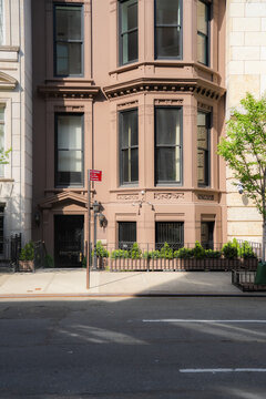 View of a classic brownstone building facade with elegant bay windows and a black entrance door on a sunny street in New York, New York, United States.