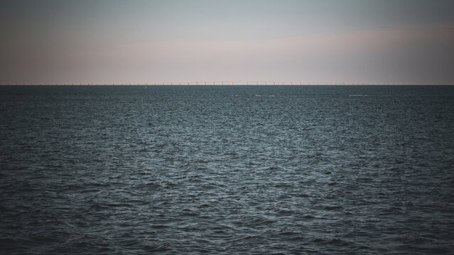 View of the Vasco da Gama Bridge stretching across the horizon over the calm Tagus River under a soft hazy sky in Lisboa, Portugal.