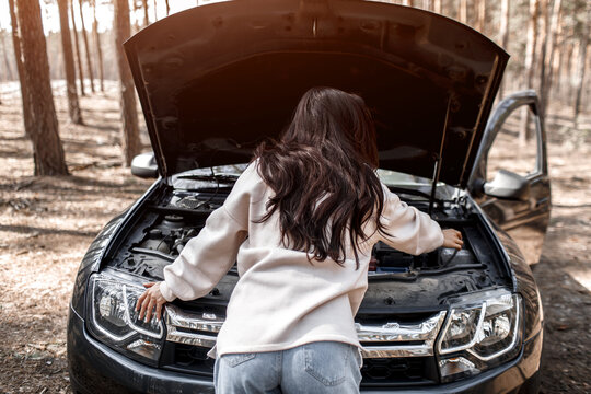 The car broke down. Accident on the road. A woman opened the hood and checks the engine and other details of the car