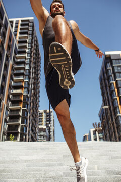 Young man exercising outside. Low view up of sporty athletic guy jumping over camera. Hands wide open. Athletist exercising. Vertical picture.