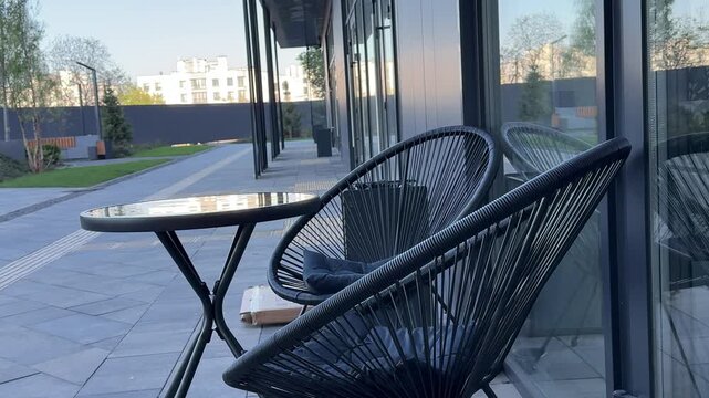 Modern outdoor cafe terrace with two black woven chairs and round glass folding table in cozy summer street coffee shop atmosphere