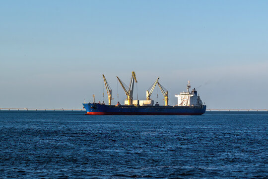 View of a large blue cargo ship with yellow cranes sailing on the Tagus River with the Vasco da Gama Bridge in the background Barreiro, Setubal, Portugal.