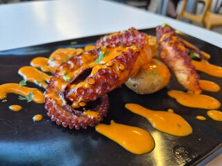 Grilled octopus with sauce on black plate © Studio-M