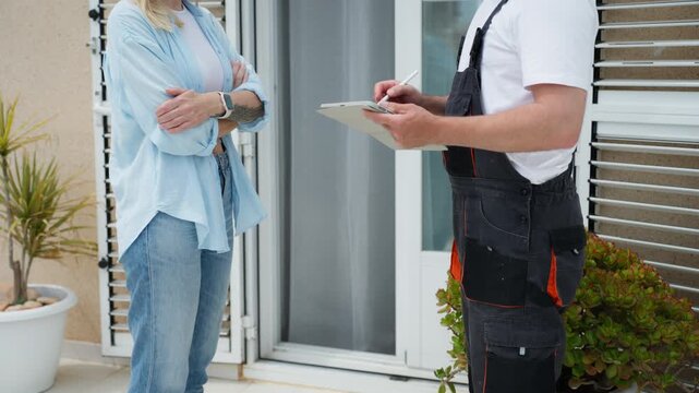 Woman signs repair contract with handyman using digital tablet for e-signature on terrace. Home maintenance agreement, digital workflow, and professional service approval concept.