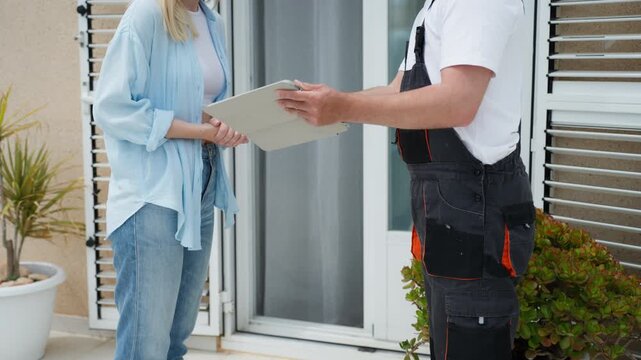 Female client providing an electronic signature on tablet for handyman after home maintenance service. Craftsman in overalls hold device for customer at front door