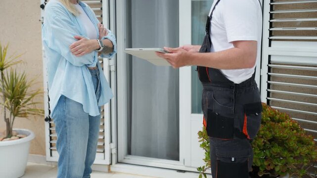 Woman standing on house terrace signs digital repair contract on technician&rsquo;s tablet. Home maintenance service, agreement process, and professional consultation concept.