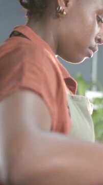 Vertical video: Pulling camera in, African woman in green apron reaching across bar, making drink
