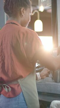 Vertical video: Turning wand on, barista in apron frothing milk with pitcher on machine for drinks