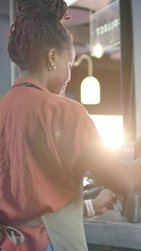 Vertical video: Turning steam, barista with green apron steaming milk for latte at cafe, espresso