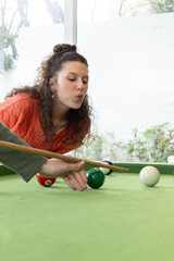 Naklejka premium Adult female with partner's bridge leaning over pool table at home aiming cue in orange sweater