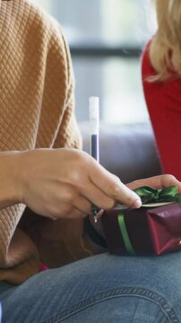 Vertical video: Noticing tag, woman in tan sweater untying ribbon on sofa opening gift with pen