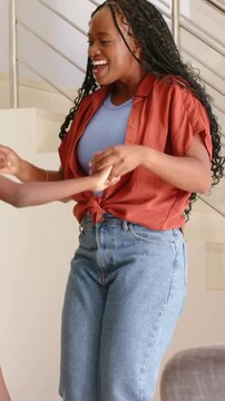Vertical video: Guiding child by hand, woman in rust top twirling child at home by plant for play