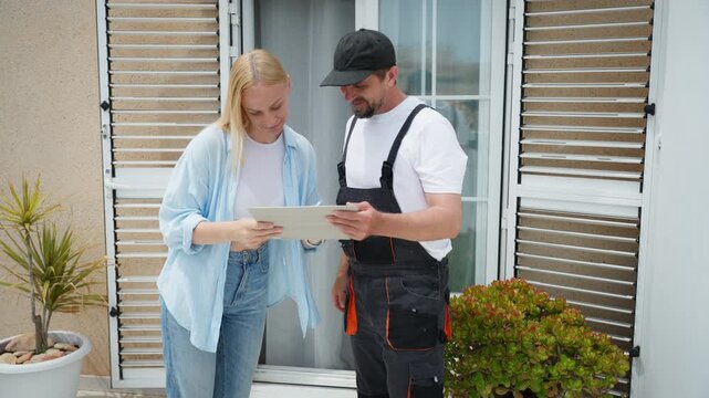 Young female homeowner signs digital service contract on tablet presented by male technician in uniform. Professional agreement finalization with friendly handshake concept.