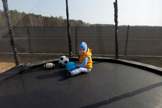 Toddler boy playing with balls on trampoline outdoors
