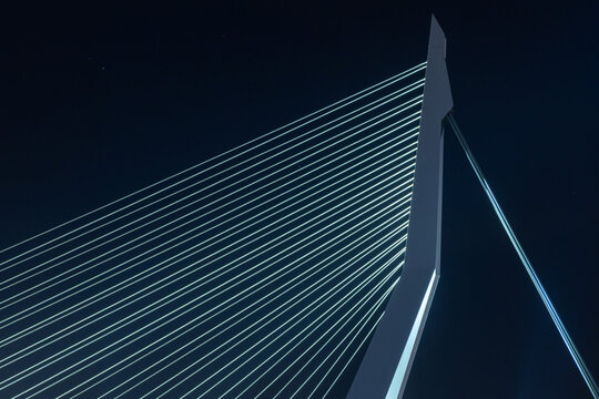 View of the Erasmusbrug bridge featuring its illuminated white pylon and stay cables against a dark night sky in Rotterdam, Zuid-Holland, Netherlands.