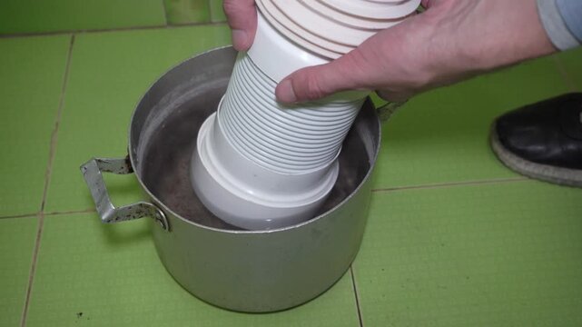 plumber softens corrugated pipe for easier installation in hot water, How to make corrugated pipe soft, Plumber prepares a flexible drain pipe for installation by softening the plastic with heat