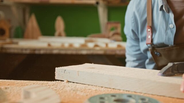Close-up view of unknown craftsman brushing sawdust off wooden plank during workday in carpentry workshop