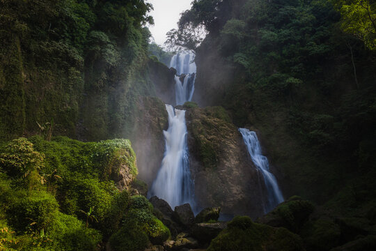 View of Curug Sewu Waterfall cascading through lush tropical greenery and mist in Kecamatan Patean, East Java, Indonesia.