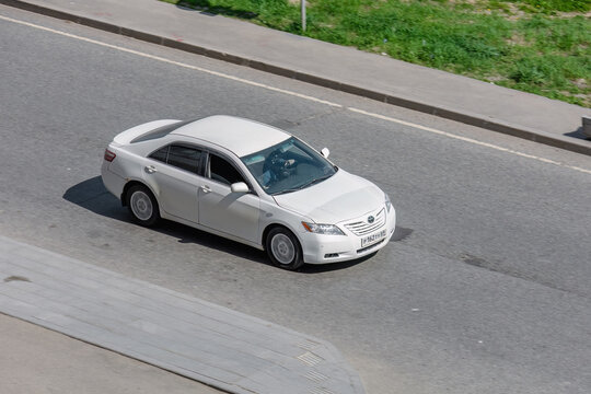 white Toyota Camry sedan driving on a paved road. Urban road environment