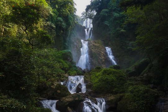 View of the multi-tiered Curug Sewu Waterfall cascading through lush tropical forest and dense green vegetation in Kecamatan Patean, Central Java, Indonesia.