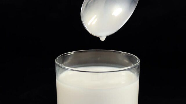Metal spoon transfers black boba pearls into a glass of milk over dark surface with fluid motion and soft contrast within beverage preparation context