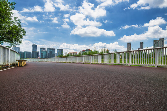 A scenic park pathway leading towards a modern city skyline under a bright blue sky with fluffy white clouds