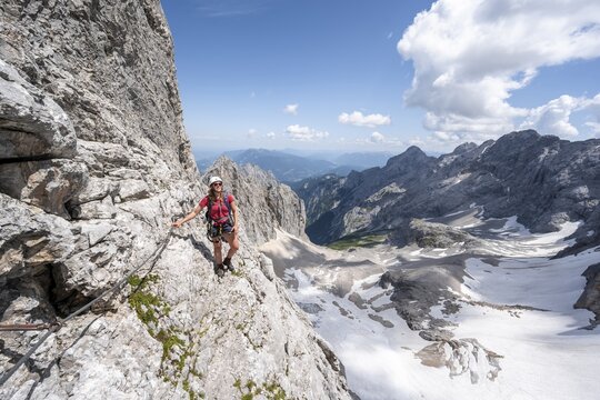 Mountaineer with helmet in a secured via ferrata, Zugspitz via ferrata, ascent to the Zugspitze, view of mountain basin with snowfield of the H&ouml;llentalferner and H&ouml;llental, Wetterstein range, Bavaria, Germany
